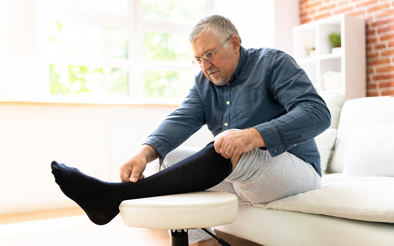 Äldre man som klär på sig stödstrumpor, Ikääntynyt mies pukee tukisukat